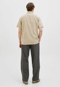 Camicia beige a maniche corte con un motivo geometrico, abbinata a pantaloni grigi larghi. La camicia presenta una linea dritta e colletto.