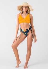 Orange bikini top with a V-neck design, paired with high-waisted navy bottoms featuring a vibrant orange fruit pattern and side ties.