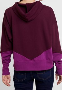 Felpa con blocchi di colore in bordeaux e viola, caratterizzata da un ampio cappuccio, spalle scese e una finitura testurizzata sul retro.