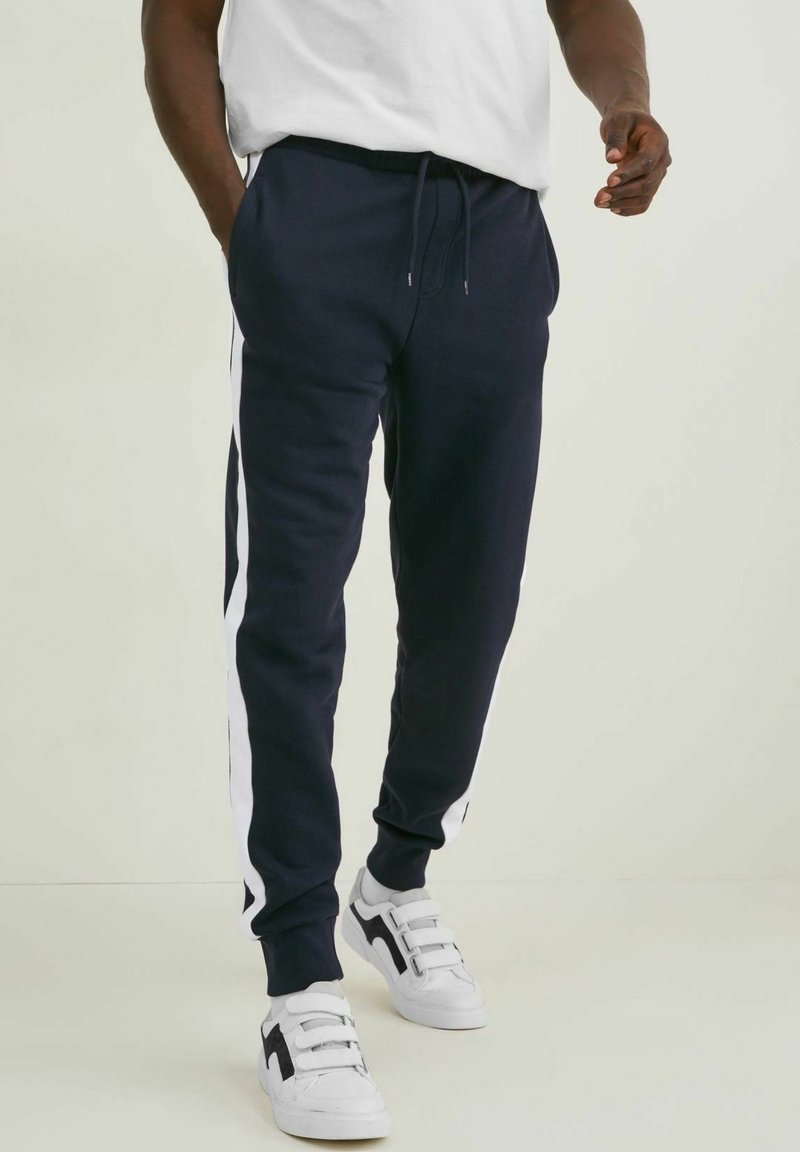 Laadun siniset kerran stretch-housut, joissa on valkoiset sivunauhat, nyörivyö ja kapenevat lahkeet. Asusteena valkoiset sneakerit ja yksinkertainen valkoinen t-paita.