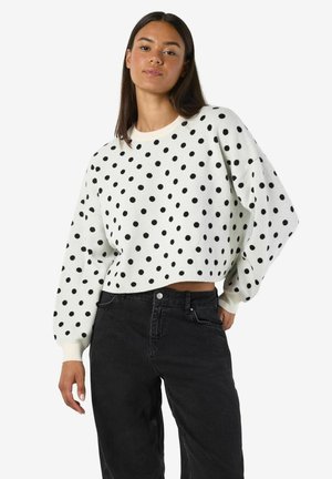 Pull blanc à pois noirs, au design court, décolleté rond, manches longues, associé à un jean noir taille haute.