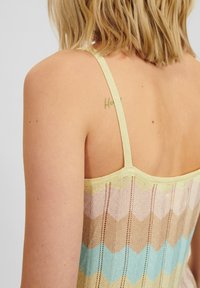 Wielokolorowy sweter na ramiączkach z wzorem chevron w pastelowych odcieniach niebieskiego, brzoskwiniowego i żółtego, z wąskimi ramiączkami i teksturowanym materiałem.