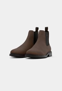 Bottes Chelsea en cuir marron avec des panneaux élastiques sur les côtés et des languettes de traction, présentant une toe arrondie et une semelle en caoutchouc texturée.