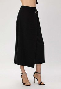 Jupe midi noire avec un design en drapé, dotée d'un détail de boucle en anneau argenté à la taille et d'un tissu lisse et texturé.
