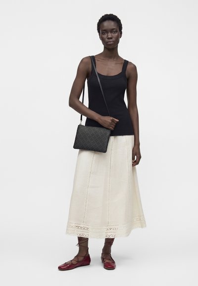 Femme portant un débardeur noir, une jupe crème longueur cheville avec des détails en dentelle, des ballerines rouges à lacets et un sac bandoulière matelassé noir.