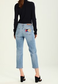 Jeans azzurri chiari a vita alta con un fit cropped e una patch unica sulla tasca posteriore. Indossati con un top nero e tacchi alti.