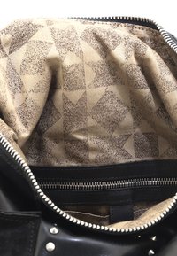 Schwarze Lederhandtasche mit einem Innenfutter aus beigem Stoff mit geometrischen Mustern. Reißverschluss oben und eine separate Reißverschlusstasche im Inneren.