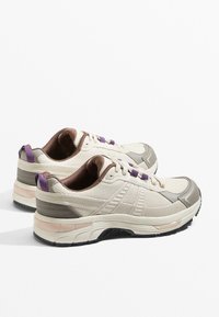 Béžové tenisky s textúrovaným zvrškom z umelej kože, hnedými akcentmi, fialovými šnúrami a silnou bielou medzipodrážkou. Obsahujú zaoblenú špičku a polstrovanú podšívku.