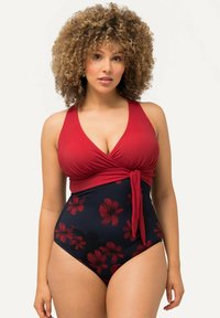 Maillot de bain une pièce avec un haut rouge enwrap avec un bas bleu marine orné de motifs floraux rouges vifs. Texture lisse, détail de taille nouée.