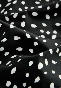 Svart tyg med en slät textur, prytt med ett spritt mönster av vita prickar i varierande storlekar. Designen är modern och djärv.