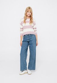 Pull rayé de couleurs rose pâle et blanche, associé à un jean en denim bleu large et des baskets blanches. Textures lisses tout au long.