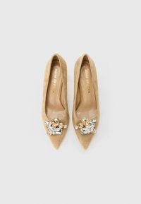 Beige suede pointed-toe flats with large clear and amber gemstone embellishments on the front and "ALMA EN PENA" gold-label insoles.