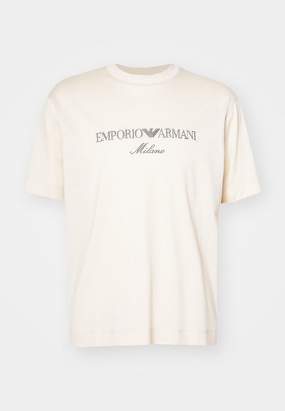 Cremefarbenes Baumwoll-T-Shirt mit kurzen Ärmeln, das ein silbernes gesticktes Logo zeigt, das "EMPORIO ARMANI Milano" auf der Vorderseite trägt.
