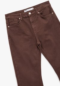 Ruskeat farkut slim-fit-mallilla, joissa on taskut, hopeanväriset yksityiskohdat ja sileä pinta. Tagi näyttää koon 36.