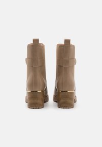 Bottines beige en cuir lisse, avec un design structuré, un talon empilé rehaussé d'or et des tirettes latérales doubles.