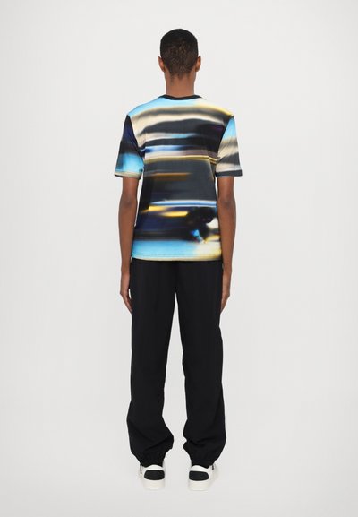 Short-sleeve, fitted T-shirt featuring a multicolored abstract pattern. Black collar and sleeves. Paired with loose black pants and white sneakers.