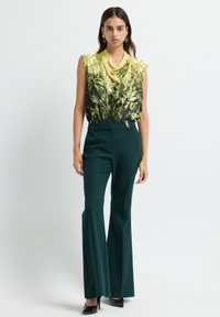 Mouwloze blouse met een groene bloemenprint, gecombineerd met donkergroene op maat gemaakte flared pants, met een ritsaccent en een gladde stof.