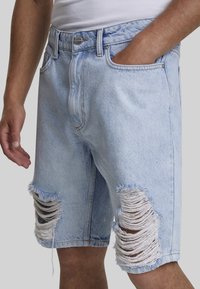 Lyst blå denimshorts har ribbede detaljer ved knæene, frynset kant, et traditionelt fem-lommer design og en knaplukning.