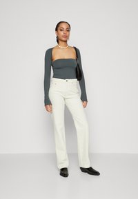 Top ajustado de manga larga en gris oscuro combinado con unos pantalones vaqueros blancos de tiro alto y pierna ancha. La modelo lleva un bolso negro y botas negras hasta el tobillo.