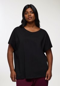 Czarna, oversize koszulka wykonana z miękkiej bawełny, z okrągłym dekoltem i krótkimi rękawami. Gładka faktura bez widocznych wzorów czy akcentów.