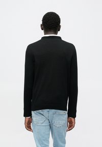 Suéter negro de manga larga con cuello, hecho de material de punto, usado sobre jeans azul claro, con una textura suave y diseño ajustado.