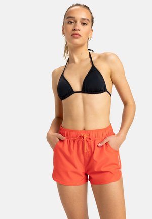 Fekete háromszög bikini felsőrész és narancssárga fürdőnadrág, elasztikus derékkal, húzózsinórral és zsebekkel, semleges háttérrel.