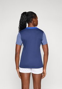 Navy blue athletic shirt with short sleeves, blue collar detailing, and a smooth texture, paired with white shorts.