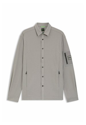 Graues Langarmhemd mit durchgehender Knopfleiste, zwei Brusttaschen und einer Reißverschlusstasche am Ärmel. Strukturiertes Gewebe und kontrastierende schwarze Beschläge.