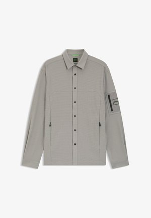 Graues Langarmhemd mit durchgehender Knopfleiste, zwei Brusttaschen und einer Reißverschlusstasche am Ärmel. Strukturiertes Gewebe und kontrastierende schwarze Beschläge.