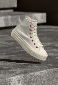 Λευκό πανί ανδρικό sneaker υψηλού τύπου με κόκκινους οφθαλμούς και κορδόνια πάνω από υφή σκυροδέματος στα σκαλιά και το έδαφος.