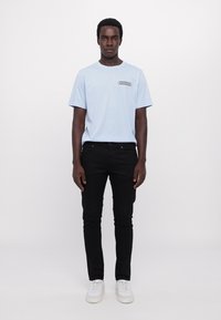 Lyseblå bomulds t-shirt med rund hals, korte ærmer og farverigt logo på brystet, parret med sorte slim-fit jeans og hvide sneakers.