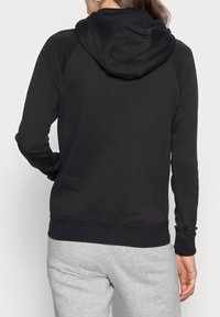 Svart huvtröja med dragsko, ribbade muddar och midja, tillverkad av mjukt material; matchad med ljusgrå sweatpants.