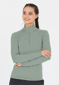 Lys grøn langærmet skjorte med halv-zip krave, tætsiddende design og glat tekstur. Sømdetaljer giver et struktureret udseende.