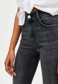 Jeans de mezclilla elásticos en gris oscuro con un diseño ajustado, que presentan un bolsillo delantero, herrajes de remache y una textura suave.