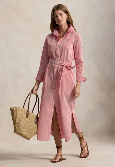 Μακριά ριγέ φόρεμα πουκάμισο σε κόκκινο και άσπρο με κουμπιά, γιακά και ζώνη. Συνδυασμένο με πλεκτή τσάντα ώμου και σανδάλια με λουράκια.