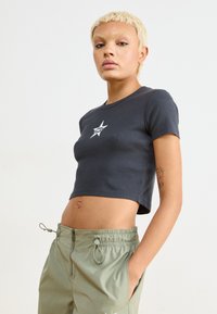 Svart cropped t-shirt i ribbat tyg med korta ärmar och vit stjärnlogotyp på bröstet, tillsammans med ljusgröna byxor med dragsko.