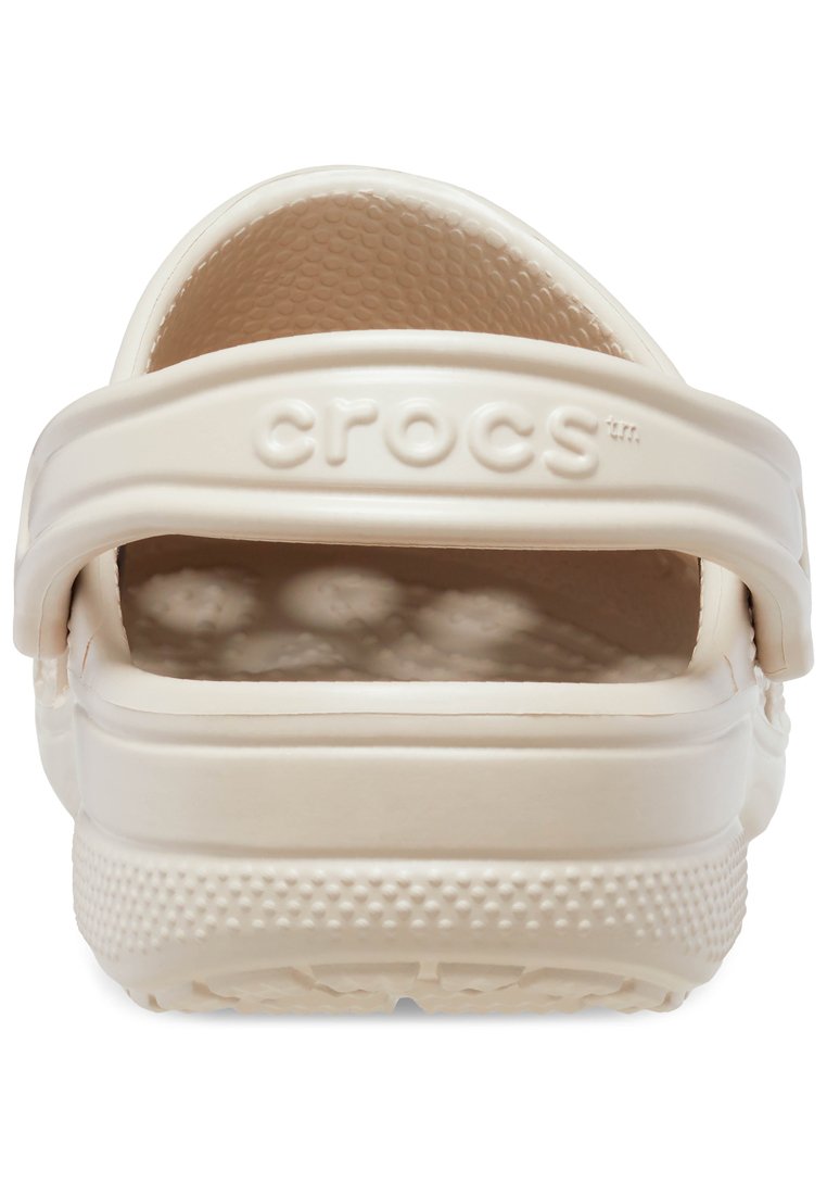 Crèmekleurige Crocs met een achterband, een gestructureerde binnenkant en afvoergaatjes. De buitenzool heeft een gepattern grip voor tractie.