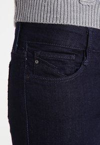 Mörkblå denimjeans med en sidoficka, kontrasterande sömmar och en texturerad grå stickad tröja ovanför. Rena linjer och tajt passform.