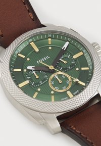 Montre à cadran vert avec un boîtier en argent texturé, des index en or et un bracelet en cuir marron. Présente des sous-cadrans et un cadran à motif détaillé.