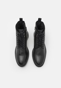 Botas de tobillo de cuero negro con un acabado texturizado, que presentan cordones, cremalleras laterales y un forro suave. Punta redonda y suela de goma plana.