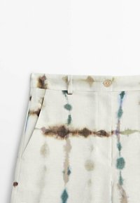 Pantalon en lin de couleur claire avec un motif tie-dye dans des tons de vert, marron et bleu. Doté d'une fermeture à boutons et de poches avant.