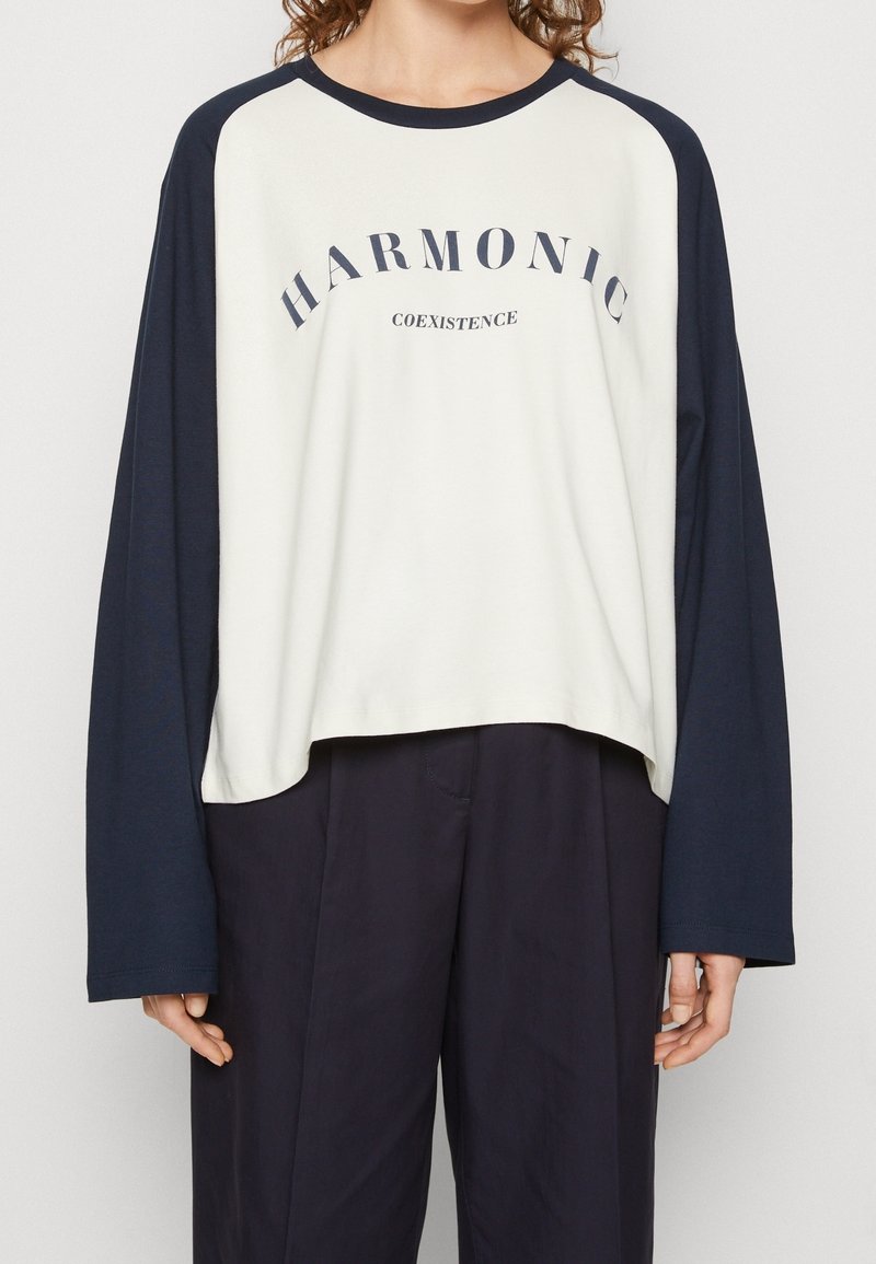 Langärmliges Raglan-T-Shirt in Creme und Marineblau. Mit "HARMONIC" und "COEXISTENCE" in Dunkelblau auf der Brust bedruckt. Aus weichem Baumwollmix.