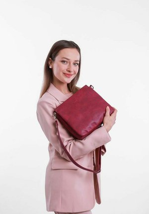 Červená kožená crossbody taška s nastavitelným popruhem, zipovým uzávěrem a vyraženým logem. Hladký povrch a obdélníkový tvar s minimálními detaily.