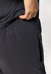 Calças desportivas pretas com um tecido suave e flexível, apresentando uma cintura elástica e um bolso lateral com fecho.