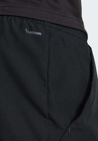 Černé sportovní šortky s texturovaným povrchem, elastickým pasem a logem "CLIMACOOL" v blízkosti kapsy. Mají štíhlý střih.