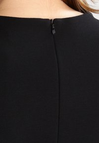 Schwarzer Stoff mit glatter Textur und einem kleinen, unauffälligen Reißverschluss hinten, der ein minimalistisches Design und klare Linien aufweist.