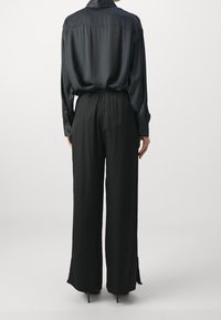 Svart satin skjorta med avslappnad passform och knäppta manschetter, tillsammans med vida svarta byxor med slitsar vid fållen.