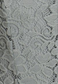 Tissu gris avec un motif de dentelle florale complexe comprenant des feuilles et des fleurs tissées avec des textures variées et des zones en résille ouverte.