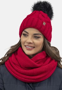 Red knitted hat with a black pom-pom, paired with a chunky red scarf, both featuring thick, textured patterns. Warm and cozy materials.