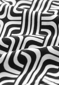 Telas en blanco y negro con un atrevido patrón geométrico de líneas entrelazadas. La textura parece suave con un ligero brillo.
